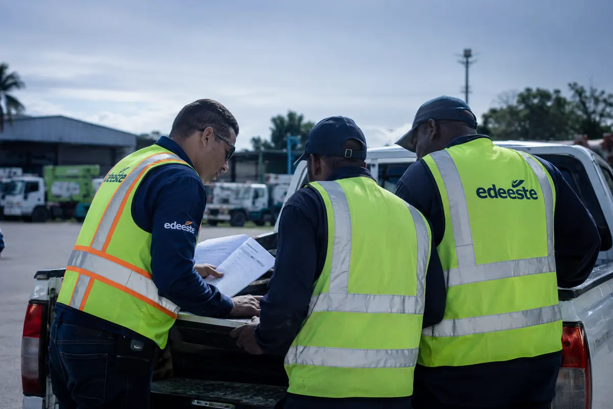 Tres trabajadores con chalecos reflectivos revisan documentación de campo sobre la batea de una camioneta, en un patio de operaciones.